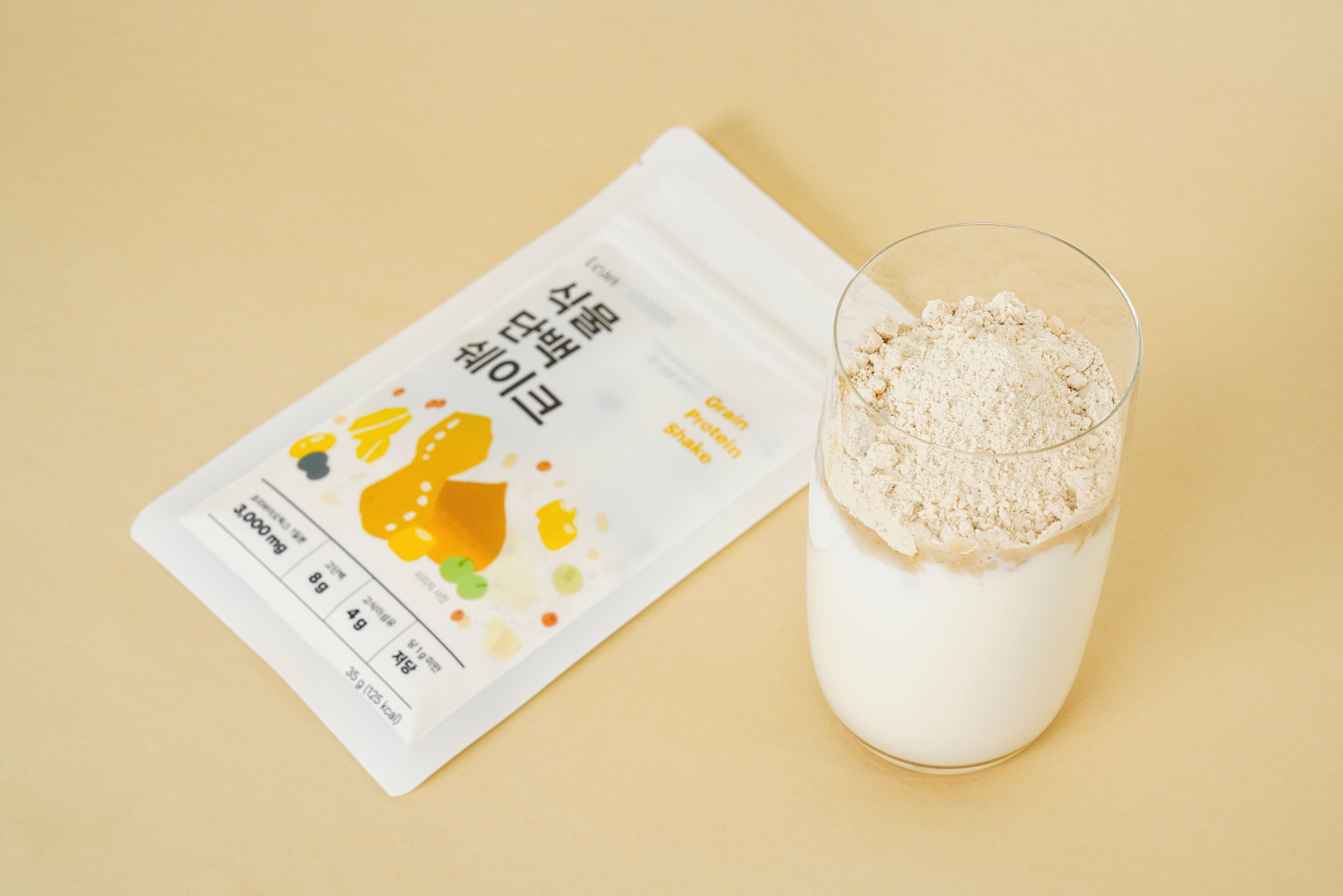 식물 단백 쉐이크 파우치와 우유를 담은 유리컵 위에 올린 가루. 포장에 35g 125kcal로 적혀 있다.